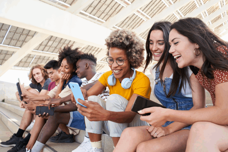 Diverse group of young adults sitting on steps, smiling and engaging with smartphones in a shared digital experience