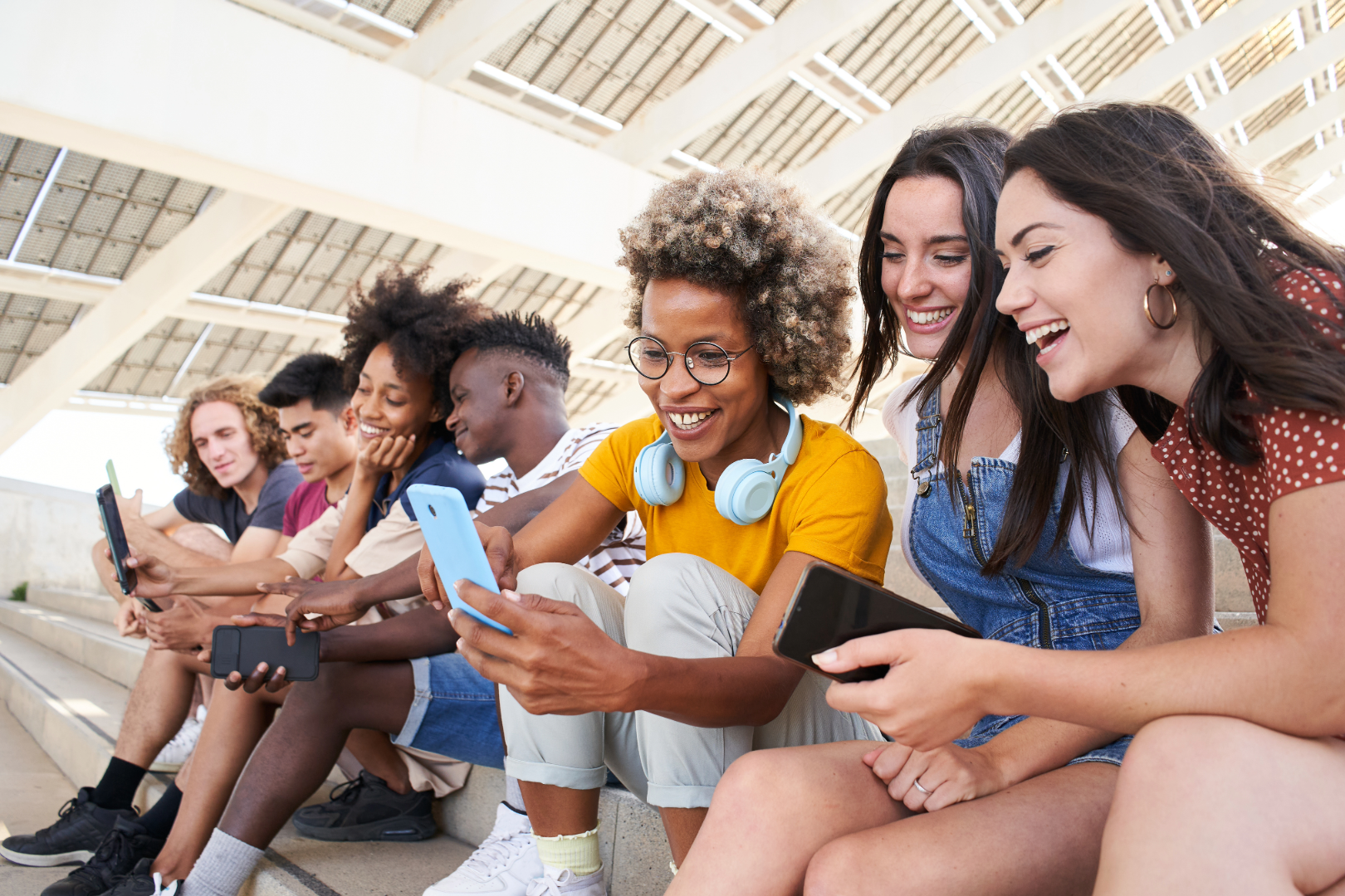 Diverse group of young adults sitting on steps, smiling and engaging with smartphones in a shared digital experience